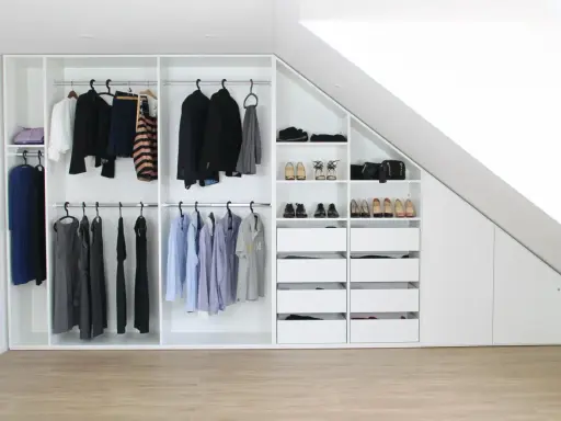 Ein maßgefertigter Kleiderschrank bauen, der sich perfekt in die Dachschräge einfügt. Ordentlich sortierte Kleidung und Schuhe.