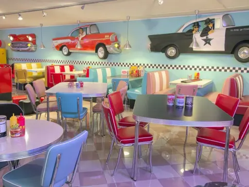 Interni di un diner in **stile americano** con sedili color pastello, tavoli cromati e decorazioni a tema auto d'epoca.