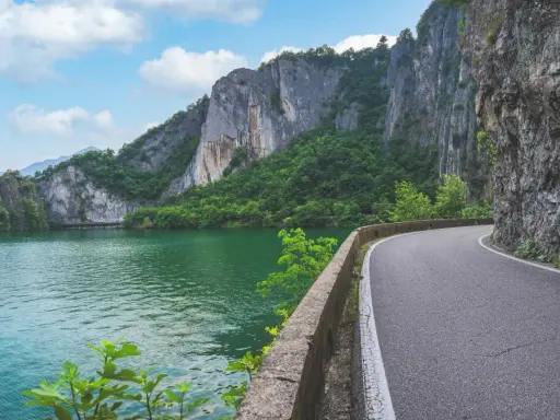 Strada panoramica lungo un lago verde smeraldo, con imponenti pareti rocciose e vegetazione lussureggiante. Un percorso suggestivo per raggiungere la baia di Bogn.