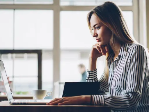 Donna pensa a come fare un webinar, seduta al laptop con una tazza di caffè.
