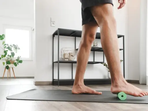 Mann rollt mit einem kleinen grünen Ball unter dem Fuß, um Plantarfasziitis-Hausmittel anzuwenden.