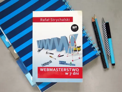 Okładka książki "Webmasterstwo w 7 dni" z grafiką WWW, narzędziami i drabiną, obok zeszytów i długopisów.