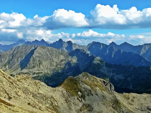 Widok z Zawratu na skaliste szczyty Tatr pod błękitnym niebem z białymi chmurami.