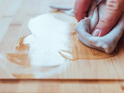 Mano limpiando pintura del suelo de madera con un trapo.