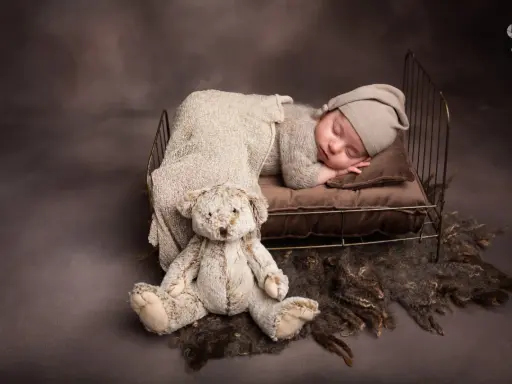Dolce bimbo appena nato dorme sereno in una culla con un orsacchiotto. Foto bimbi appena nati.