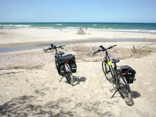Dwa rowery z sakwami na piaszczystej plaży, gotowe na odkrywanie płaskich tras rowerowych nad morzem.