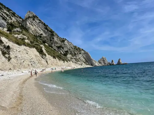 Spiaggia della Riviera del Conero con bambini che giocano e si bagnano, scogliere bianche e mare azzurro.