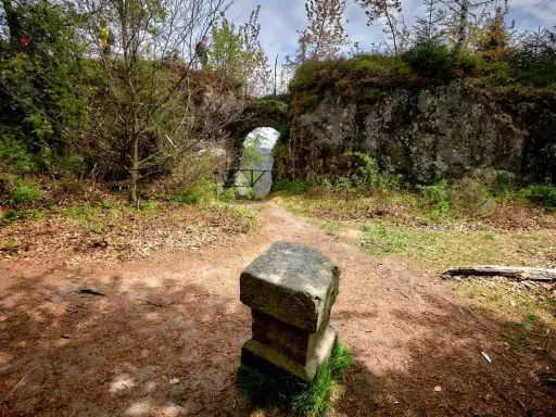 Kamienny postument przed łukiem w fort karola. Ścieżka prowadzi przez zarośla do zabytkowej budowli.