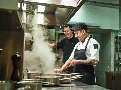 Deux chefs travaillent dans une cuisine de restaurant, respectant la norme de qualité. Vapeur s'échappant des casseroles.