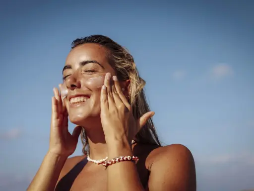 Donna sorridente applica crema solare per proteggere la pelle da macchie e tumore.