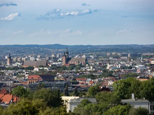 Widok na Kraków z punktu widokowego. W oddali widać kościół Mariacki i Wawel, a bliżej zabudowania miejskie i zieleń.
