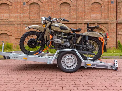 Motocykl Ural zabezpieczony pasami na przyczepie, pokazujący, jak przewieźć motocykl na zwykłej przyczepie.