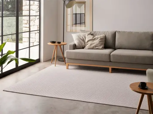 Un salón moderno con un sofá gris, una alfombra de diseño y una mesa auxiliar.