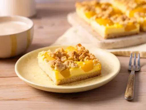 Ein Stück saftiger Pfirsich Blechkuchen mit Vanillepudding und Streuseln auf einem gelben Teller, daneben eine Gabel.