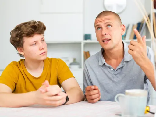 Ojciec tłumaczy synowi, jak rozmawiać z nastolatkiem, używając gestów. Chłopak słucha uważnie.