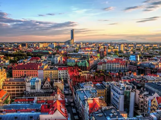Widok na Wrocław, największe miasto zachodniej Polski, z dominującym wieżowcem Sky Tower. Słońce zachodzi nad kolorowymi dachami kamienic.