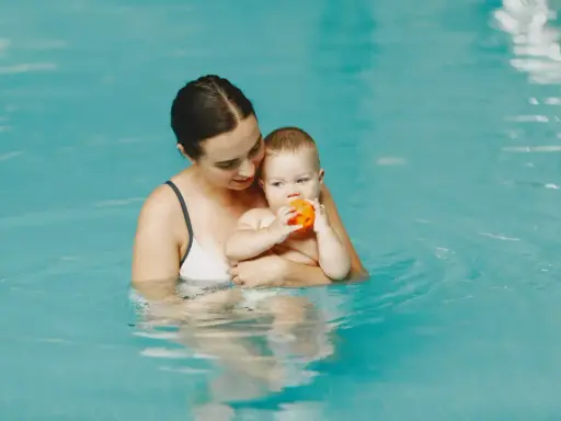 Mama trzyma roczne dziecko na basenie. Maluch bawi się pomarańczową piłeczką.
