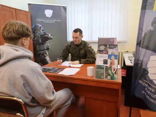 Młody mężczyzna rozmawia z żołnierzem w punkcie rekrutacyjnym. Dyskutują o możliwościach związanych z obowiązkową służbą wojskową.