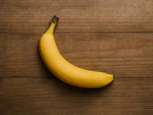 Eine gelbe Banane liegt auf einem Holztisch. Sie ist ein gesunder Snack, aber wie viel Protein hat eine Banane?