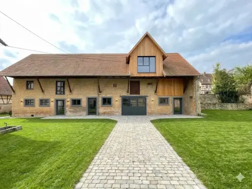Belle grange rénovée avec une façade en briques jaunes, un toit en tuiles et un ajout moderne en bois. Un chemin pavé mène à l'entrée principale.