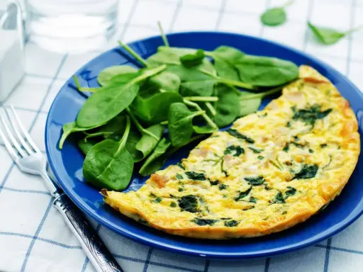 Frittata di spinaci dorata su piatto blu, accompagnata da spinacini freschi. Un pasto leggero e gustoso.