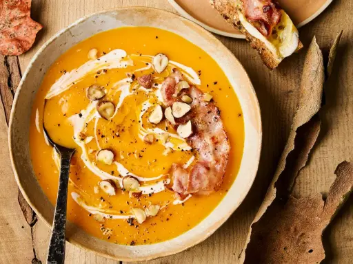 Velouté de courge onctueux, garni de noisettes croquantes, d'une touche de crème et d'une tranche de bacon croustillant. Un délice automnal qui évoque le beurre de courge.
