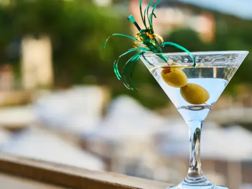 Elegancki kieliszek martini z dwiema oliwkami i zieloną ozdobą. Idealny na toast "cin cin fiero" w letni wieczór.