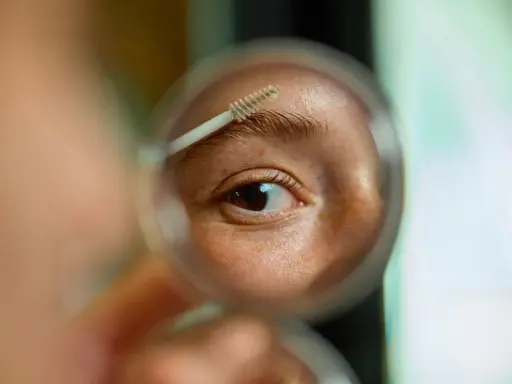 Gros plan sur un œil et un sourcil, une brosse à sourcils est utilisée pour les coiffer. La question est : est ce que les sourcils repoussent ?