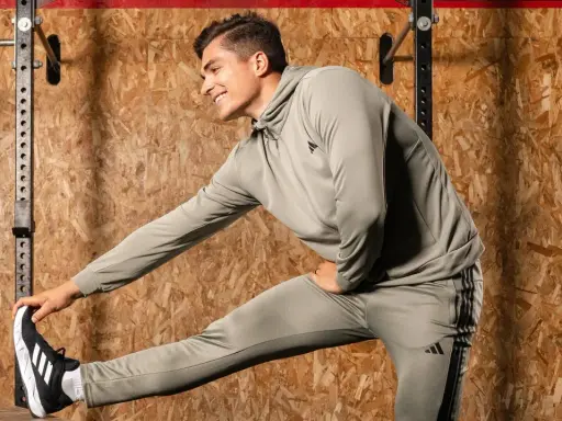 Ein Mann in Trainingskleidung macht dynamisches Dehnen vor einer Holzwand.