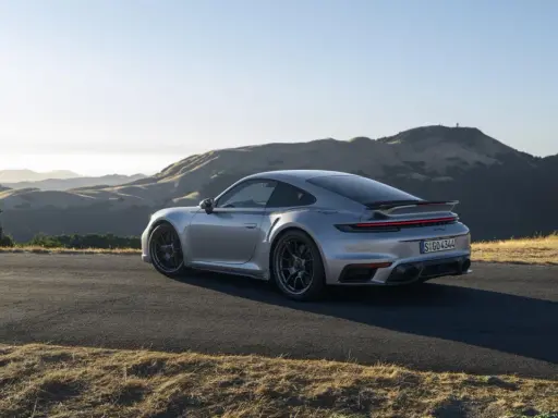 Silberner Porsche 911 Turbo S, ein Sondermodell 2023, parkt auf einer Bergstraße mit sanften Hügeln im Hintergrund.