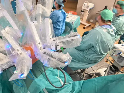 Chirurdzy w zielonych fartuchach prowadzą operację prostaty da Vinci. Robotyczne ramiona systemu są widoczne, pokryte sterylnymi osłonami.