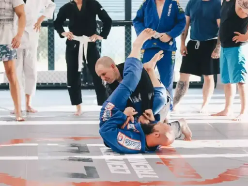 Dwóch mężczyzn w niebieskich kimonach ćwiczy chwyty na macie. To właśnie bjj co to za sztuka walki, która uczy kontroli i poddań.