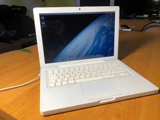 Biały, pierwszy MacBook z widokiem Ziemi na ekranie, stoi na drewnianym stole.