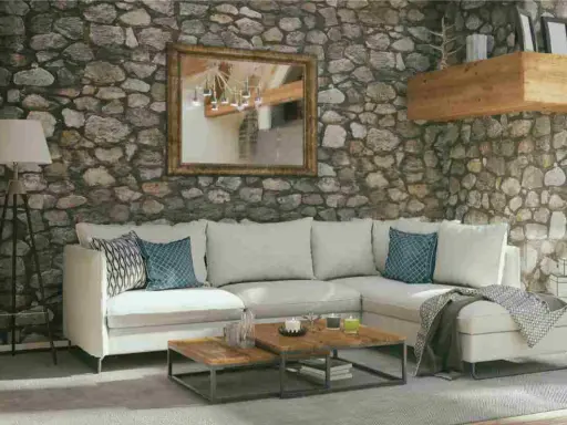 Soggiorno accogliente con pareti in pietra grezza, divano bianco, tavolini in legno e specchio dorato. Ottime idee pareti in pietra per un ambiente rustico.
