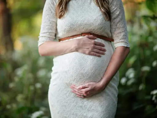 Kobieta w białej sukience obejmuje ciążowy brzuch. To piękny moment, kiedy można zajść w ciążę i poczuć nowe życie.