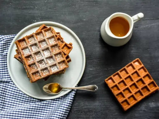 Gaufres de farine de châtaigne saupoudrées de sucre glace, servies avec du miel doré. Un délice gourmand.