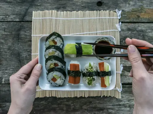 En bricka med olika sorters sushi, perfekt för ett enkelt sushi recept. En hand håller ätpinnar redo att plocka upp en bit.