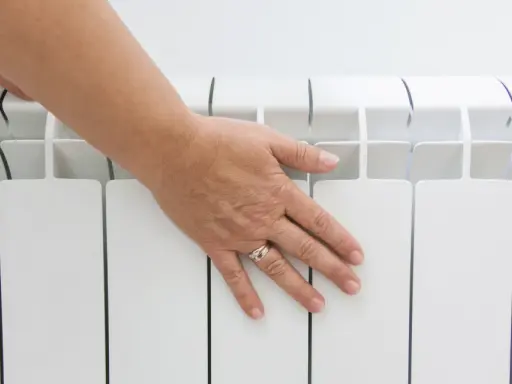 Main posée sur un radiateur électrique blanc, vérifiant la température hors gel.