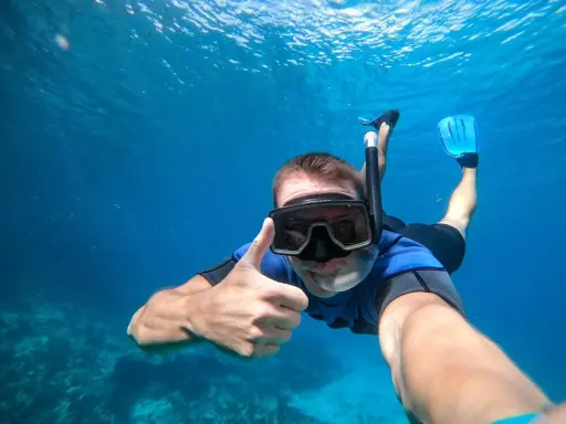 En man snorklar och ger tummen upp i det klara vattnet vid Nerja strand.