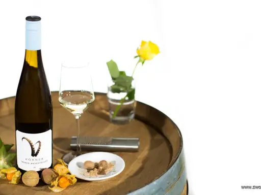 Flasche Gelber Muskateller Wein, Glas, Sternfrucht, Physalis, Litschi und Muskatnuss auf einem Holzfass.