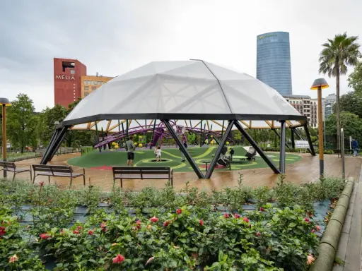 Modern playground under a geodesic dome in Parque Doña Casilda. Children play while parents relax on benches.
