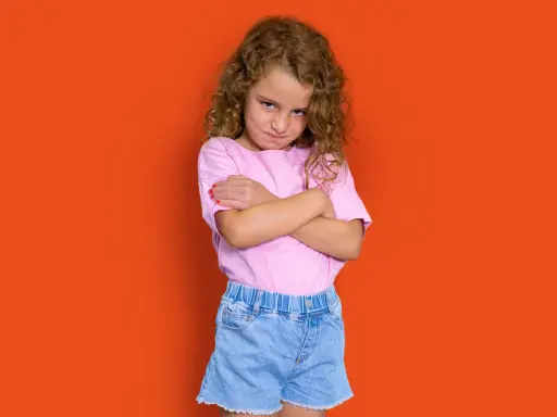 Niña con rizos, brazos cruzados y expresión de enfado. Podría representar la **depresión infantil** o simplemente un mal humor pasajero.