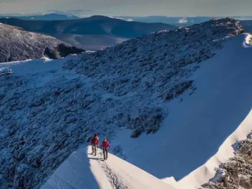 Två vandrare på en snöig bergskam med utsikt över fjällandskap. Detta är Sveriges högsta berg.