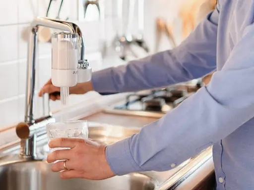 Persona llena un vaso de agua de un grifo con filtro. ¡Qué alivio, no tengo agua en casa y esto me salva!