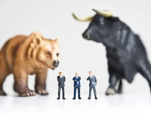 Miniature businessmen stand between a bear and a bull, symbolizing market volatility and the quest for art investment returns.