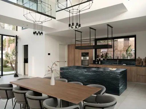 Nowoczesny salon z kuchnią otwartą: drewniane meble, czarna wyspa kuchenna, designerskie lampy i duży stół jadalniany.