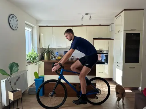 Mężczyzna w pozycji na rowerze gravel w kuchni, obok niego pies.
