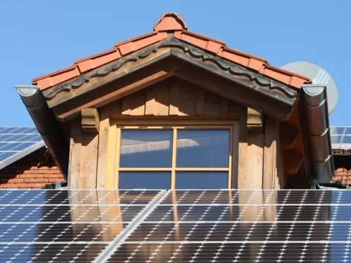 Dach mit Solarmodulen, die erneuerbare Energie von der Sonne einfangen. Ein Fenster und ein Dachüberstand aus Holz sind sichtbar.