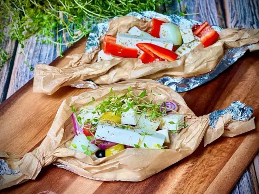 Zwei Päckchen mit Feta, Paprika, Zwiebeln und Kräutern warten darauf, gegrillt zu werden. Ein Genuss für den Gaumen!