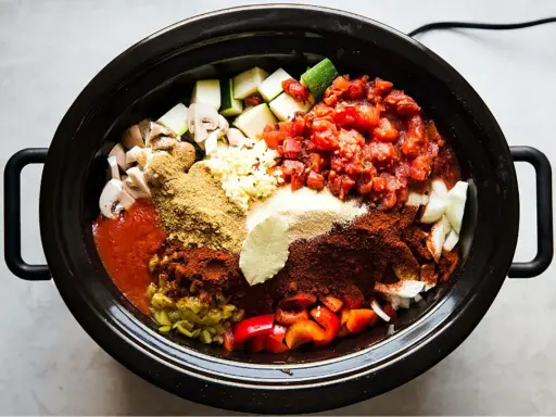 En slow cooker fylld med hackade grönsaker, tomater och kryddor, redo att bli en smakrik gryta.